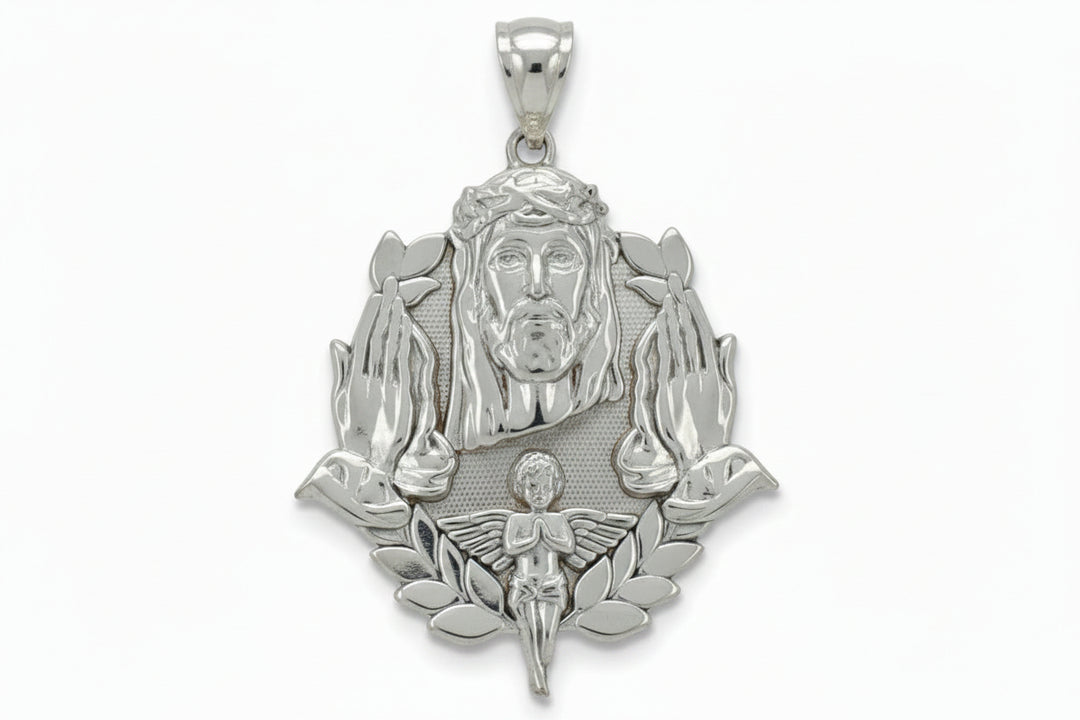 A silver pendant featuring a detailed depiction of Jesus Christ with a crown of thorns, flanked by praying hands and a small angel at the bottom, shown against a plain light gray background.